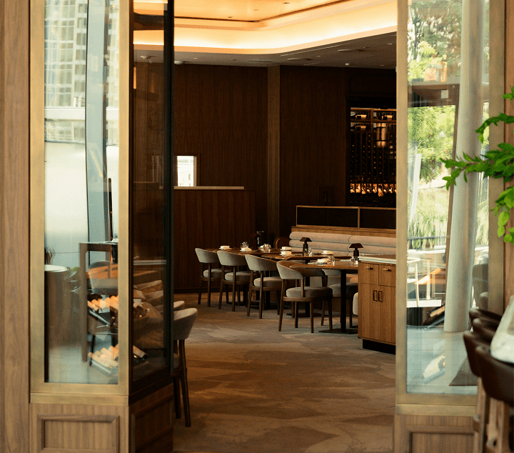 Step inside this elegant restaurant, where warm lighting and wooden interiors offer a sophisticated and inviting dining experience. Restaurant entrance showing an elegant dining area with wooden interior, set tables, and warm lighting.